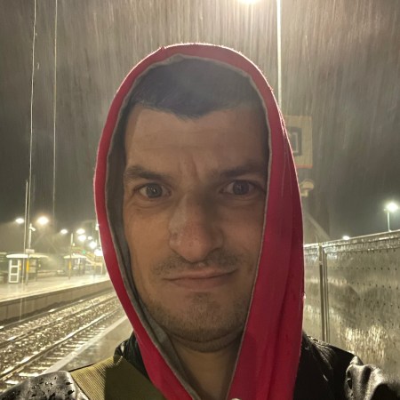 Self-portrait at Portarlington railway station at night, standing in heavy rain beneath bright platform lights.