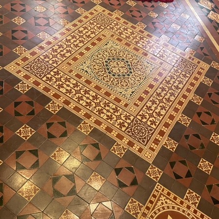 Decorative encaustic floor tiles in St John’s Church, Tralee, featuring geometric and floral Victorian patterns in red, cream, and black.