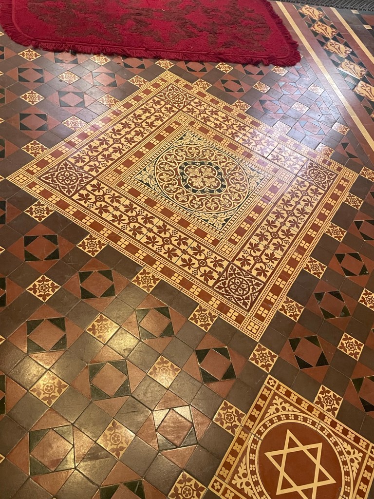 Decorative encaustic floor tiles in St John’s Church, Tralee, featuring geometric and floral Victorian patterns in red, cream, and black.