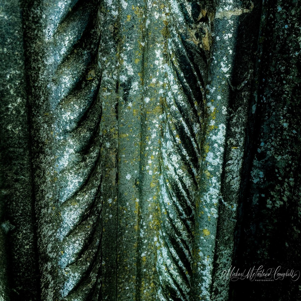 Close-up of weathered stone carved like thick twisted rope, mottled with pale and golden lichen at Clonmacnoise.